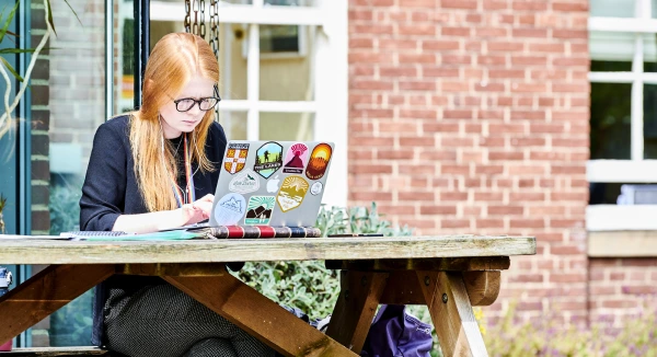 A student sat at a bench outside, while working on their laptop
